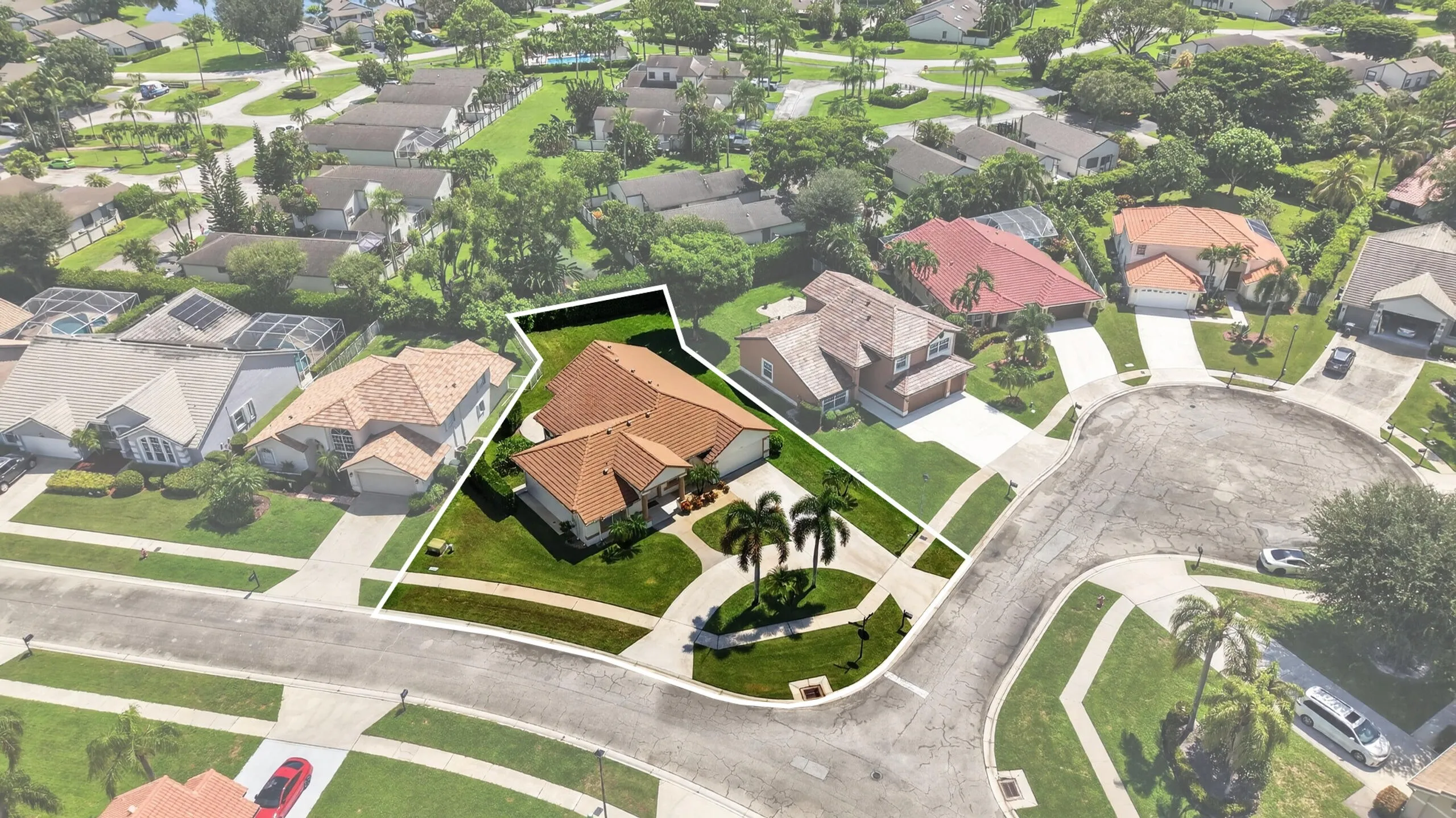 Aerial perspective featuring a red tile roof, curved driveway, mature palm trees, and a landscaped front yard