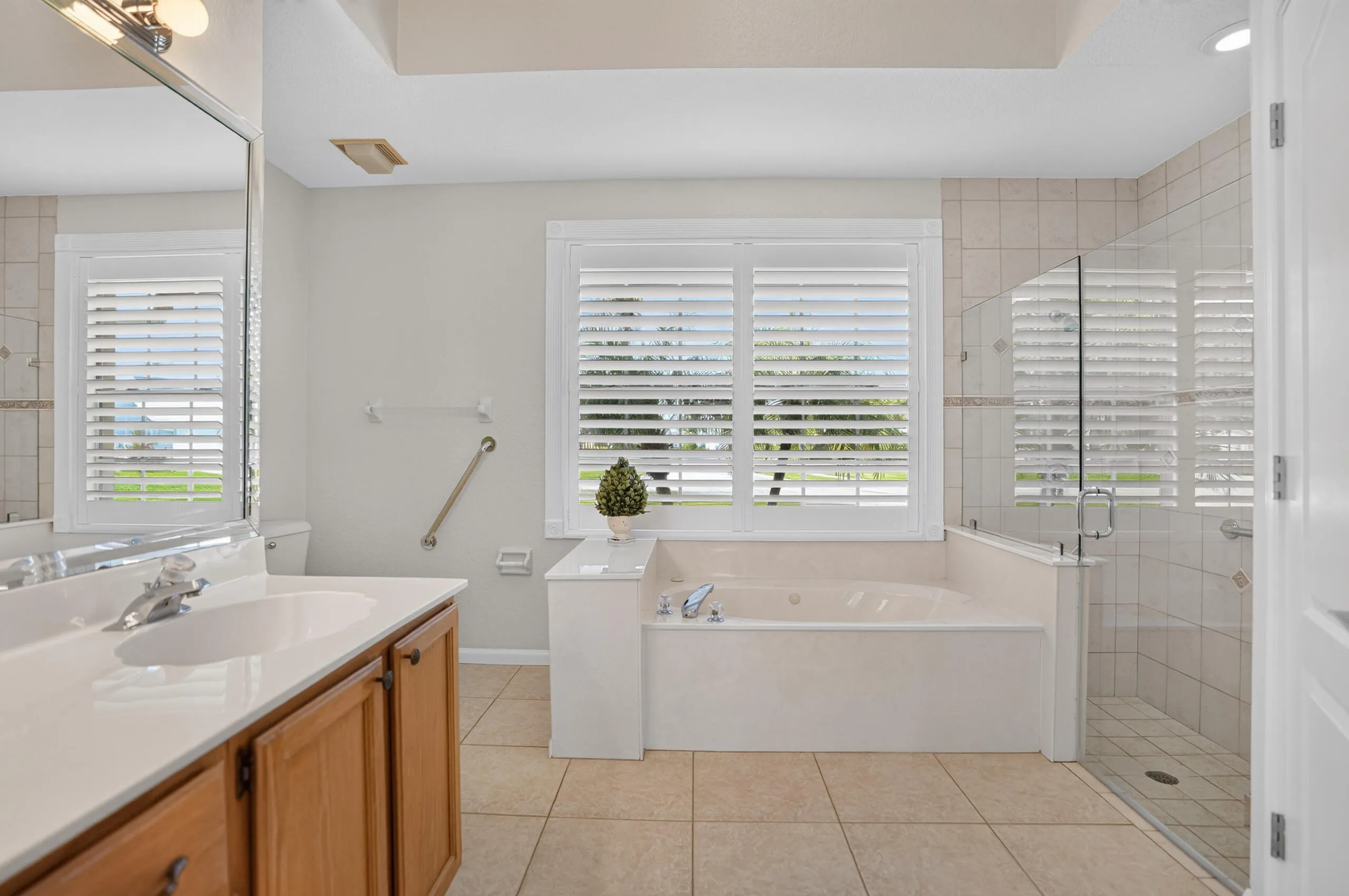 Tiled flooring, wood-finish vanity with countertop, framed mirror, built-in soaking tub, and a glass-enclosed shower