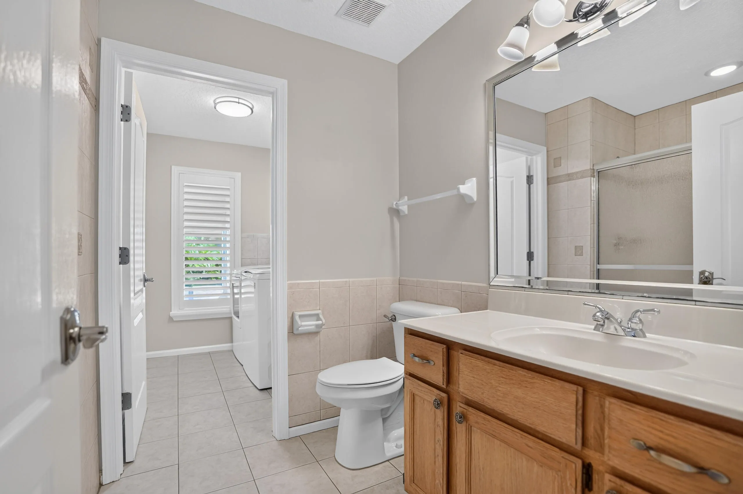 Bathroom featuring tile flooring, a wood-finish vanity with an integrated sink, a large mirror, and a tiled shower enclosure