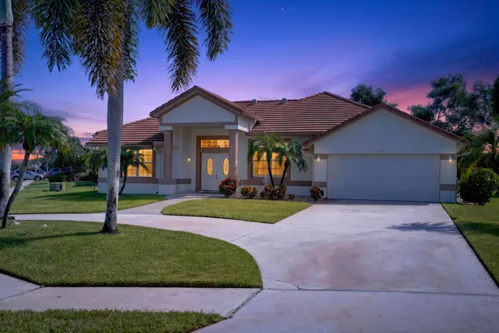 Single-story residence featuring a terracotta-style tile roof, an attached garage, a curved concrete driveway, and mature palm trees