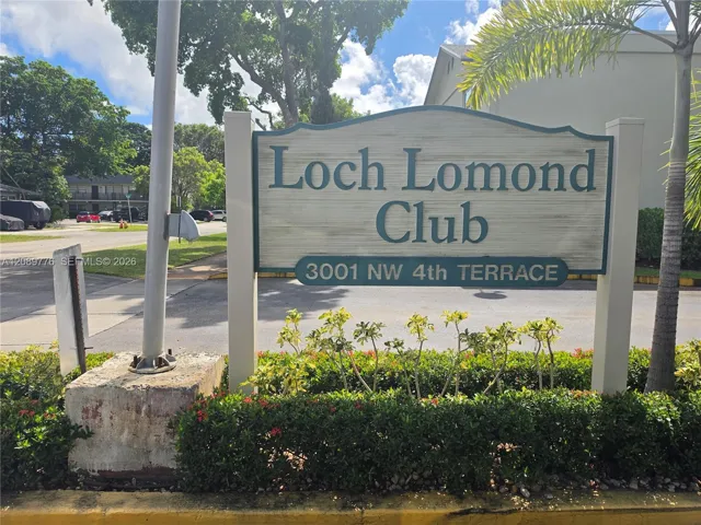 Property entrance signage featuring architectural lettering, concrete support pillars, and landscaped shrubbery