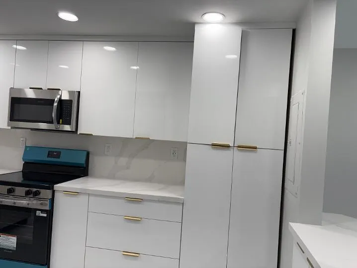 White high-gloss cabinetry with stainless steel microwave, integrated ceiling lighting, and countertops with matching backsplash