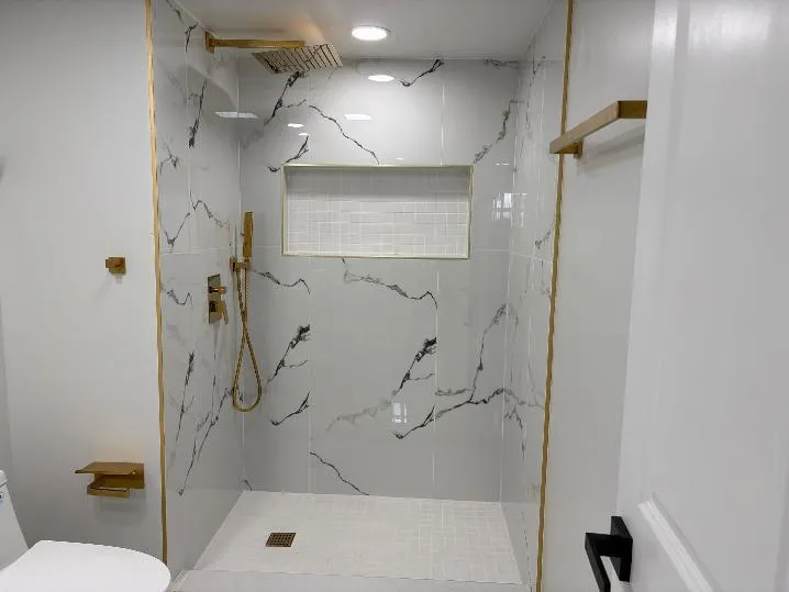 Walk-in shower featuring large format tile with dark veining, a built-in niche with subway tile, a rain showerhead, and a handheld shower attachment, all with gold-tone fixtures