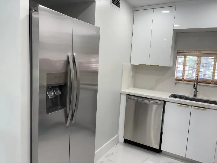 Stainless steel side-by-side refrigerator, stainless steel dishwasher, white flat-panel cabinetry with gold-tone hardware and single-basin sink with a gooseneck faucet