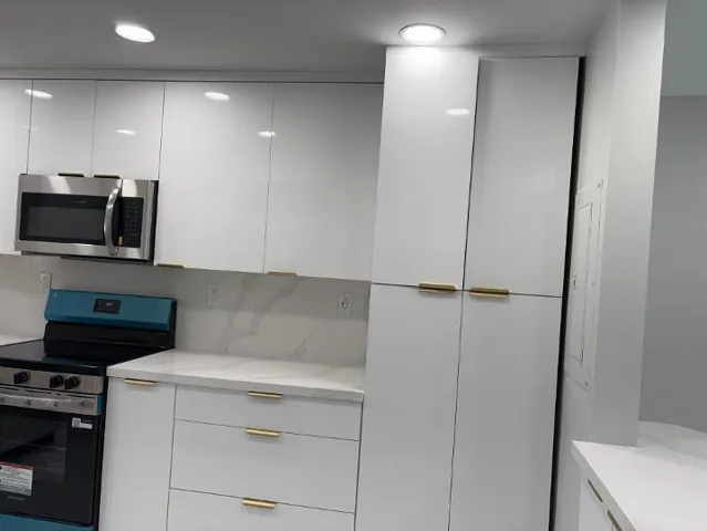 White high-gloss cabinetry with stainless steel microwave, integrated ceiling lighting, and countertops with matching backsplash