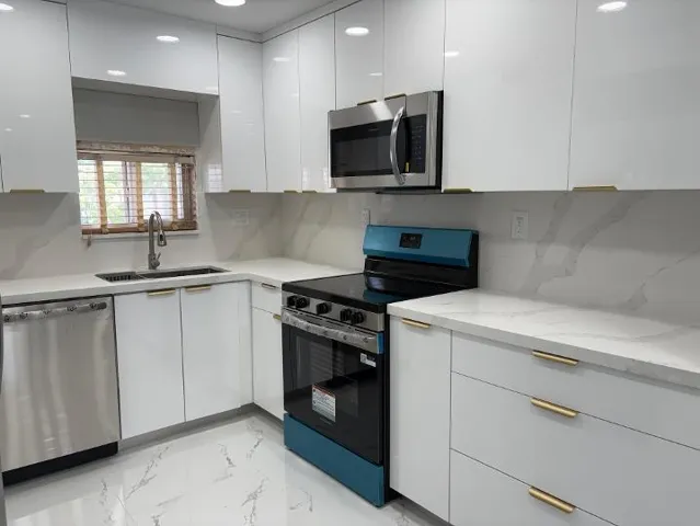 Sleek kitchen featuring white cabinetry with gold-tone hardware, quartz countertops, a stainless steel sink with a gooseneck faucet, and stainless steel appliances