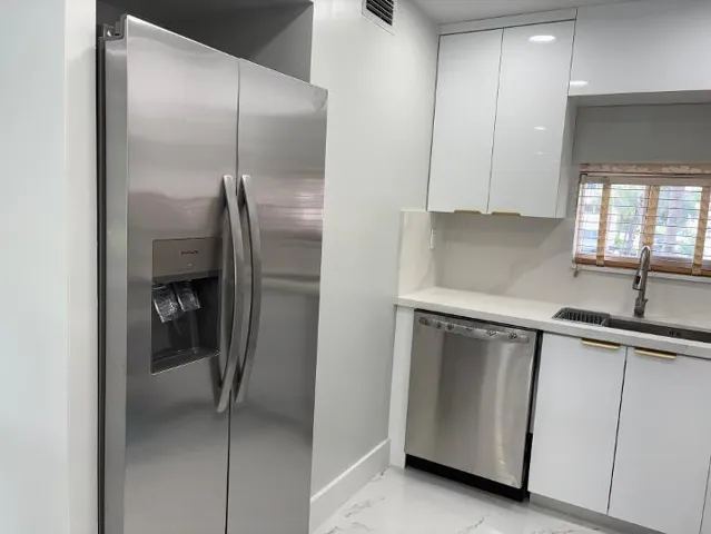 Stainless steel side-by-side refrigerator, stainless steel dishwasher, white flat-panel cabinetry with gold-tone hardware and single-basin sink with a gooseneck faucet