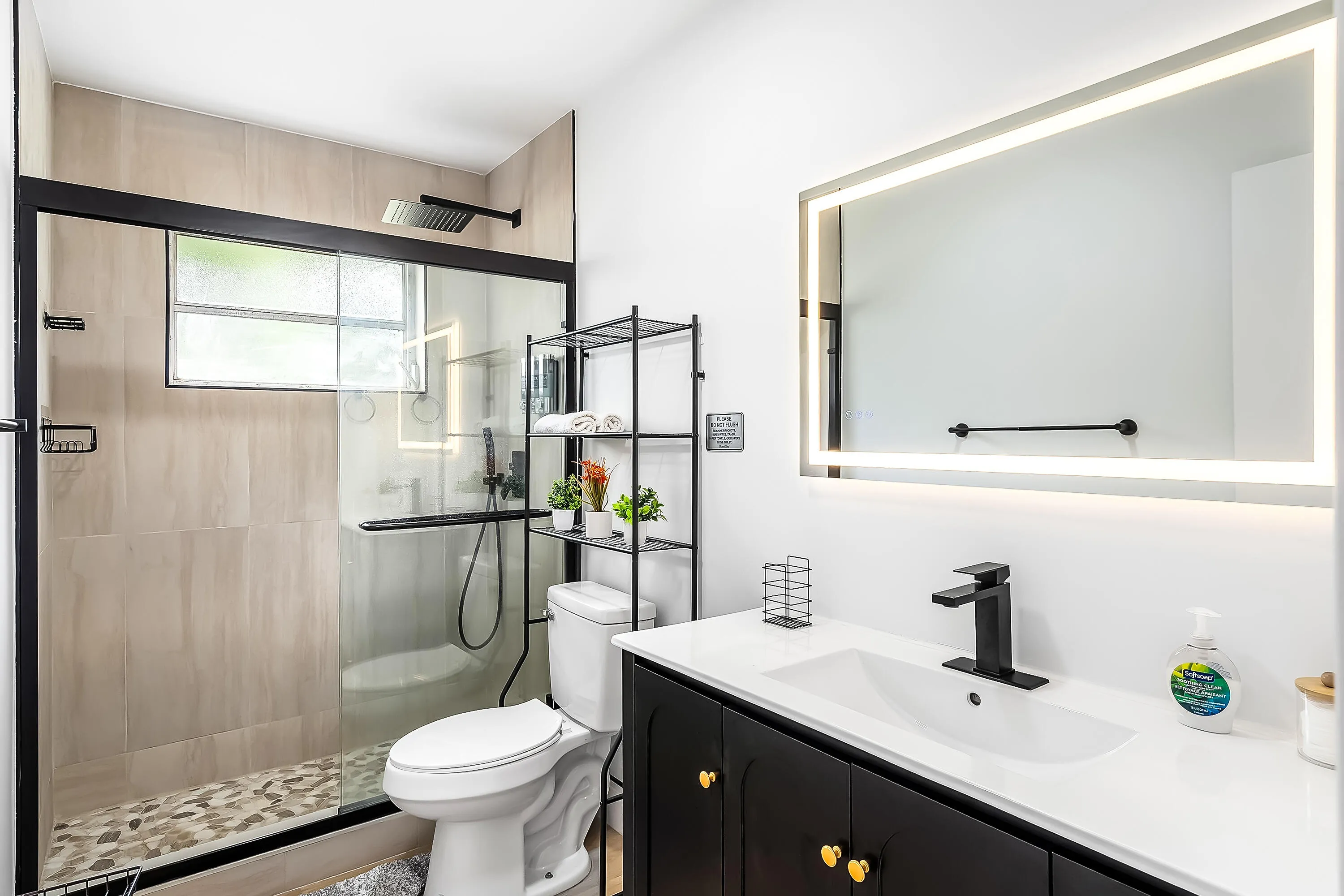 Contemporary bathroom featuring an illuminated vanity mirror, a black single-handle faucet, and a black vanity with gold-tone hardware