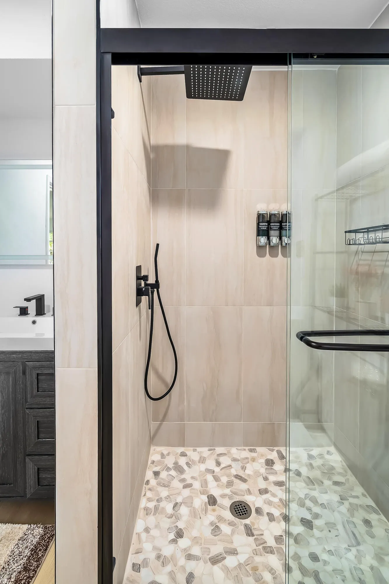 Enclosed shower with a glass door, matte black fixtures, rain showerhead, and pebble tile flooring