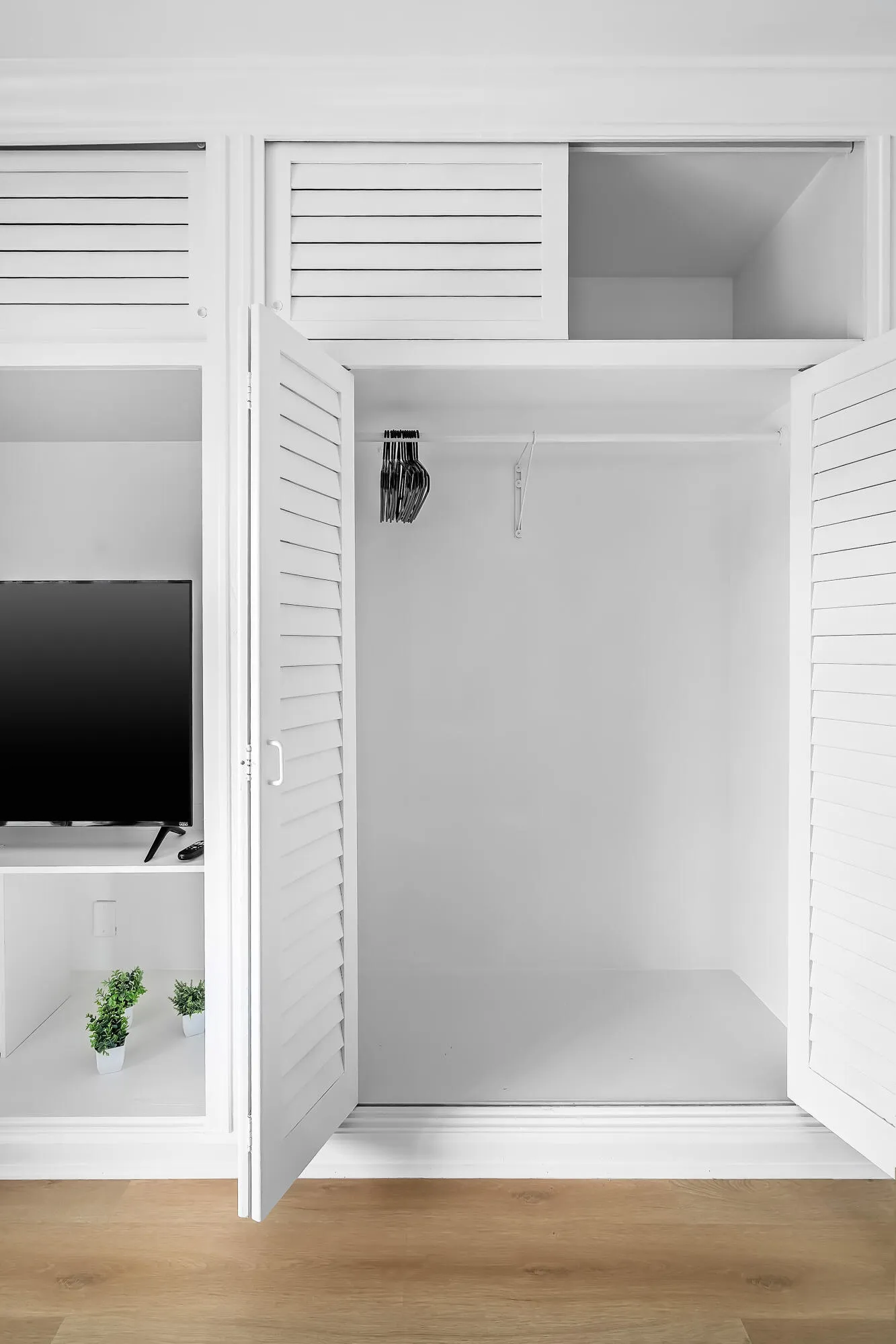Built-in white cabinetry with louvered doors, a clothes hanging rod, and integrated shelving