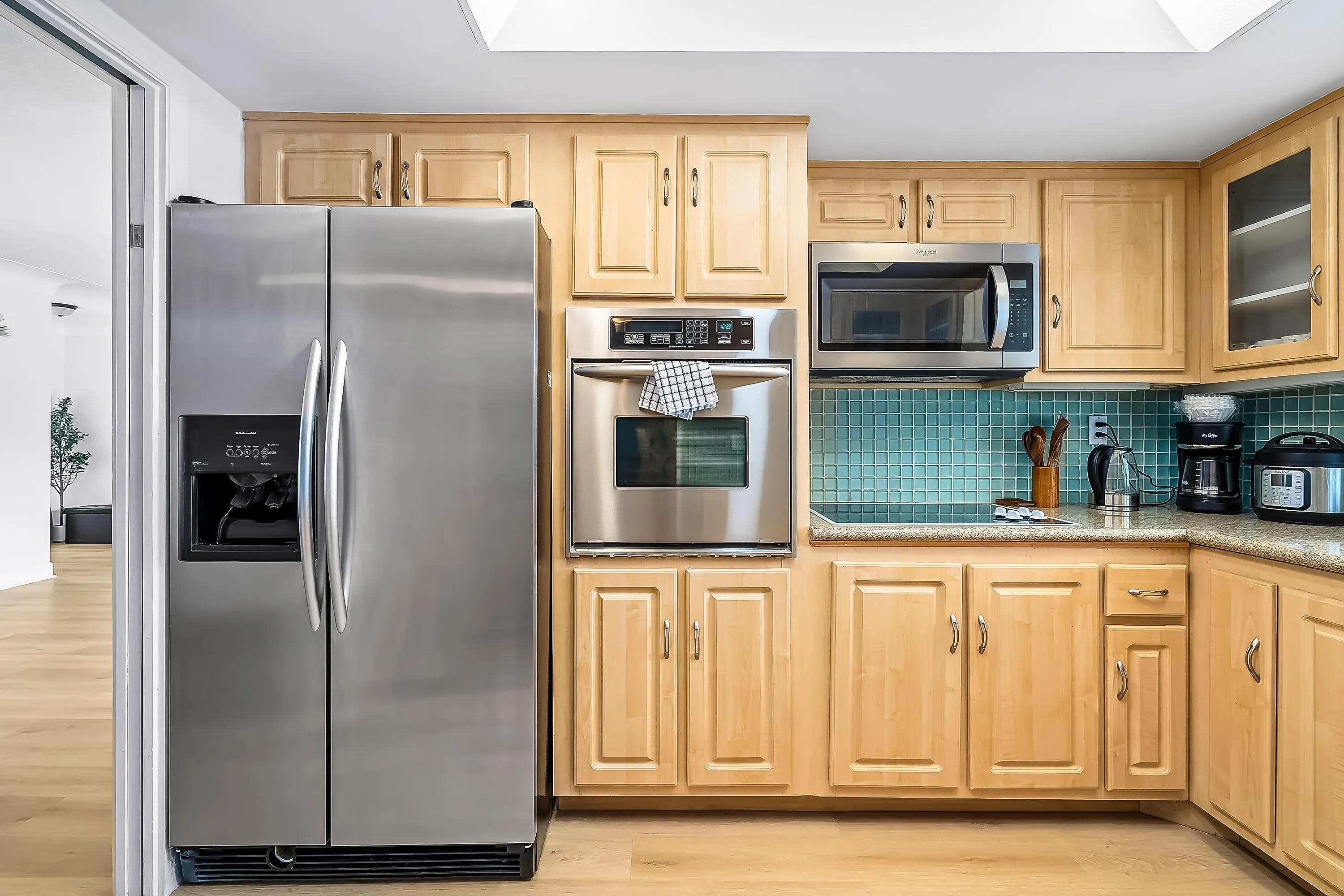 Kitchen featuring light wood cabinetry, stainless steel appliances, and a blue mosaic tile backsplash