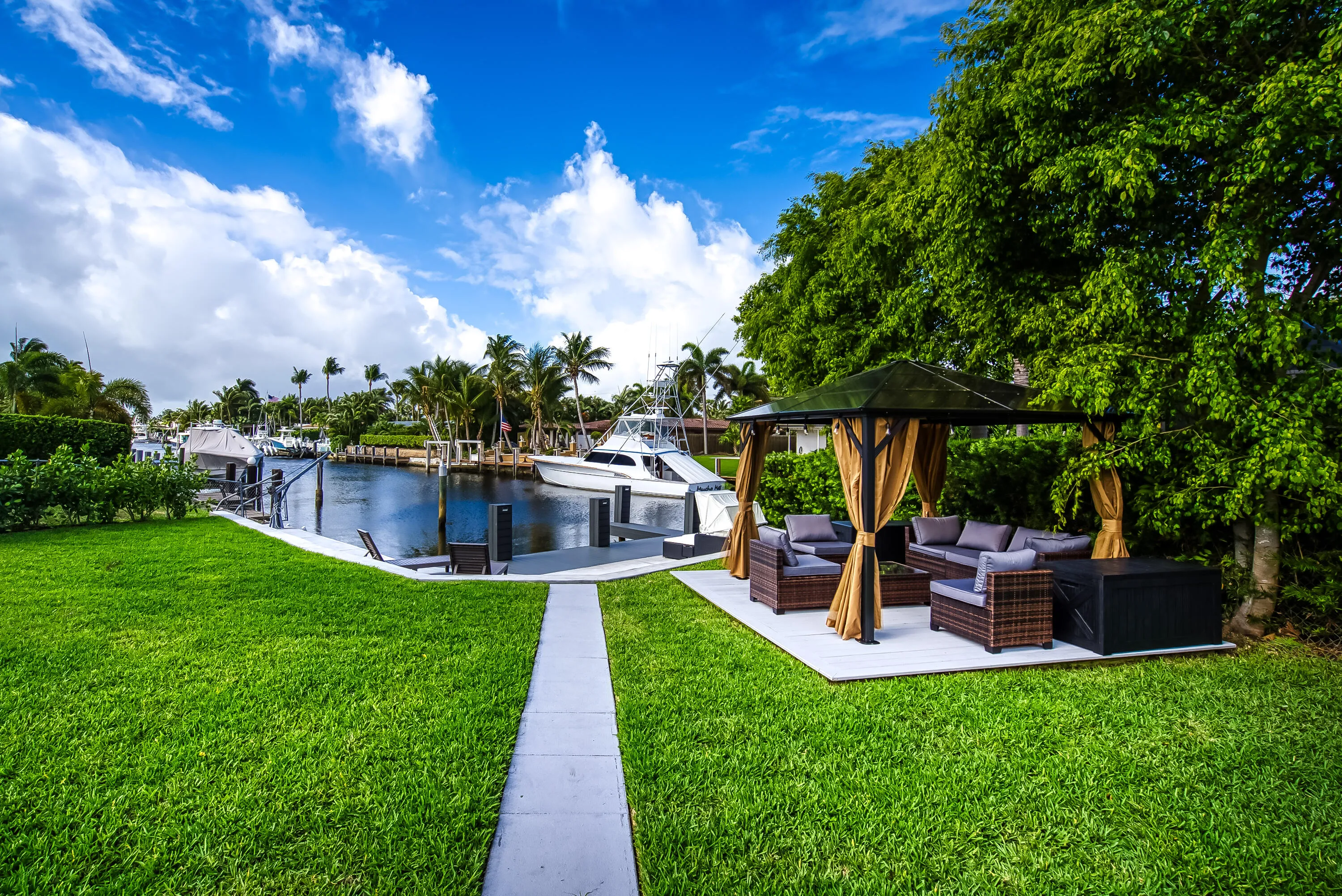 Waterside patio with a paved seating area, mature trees, manicured lawn, and dock access