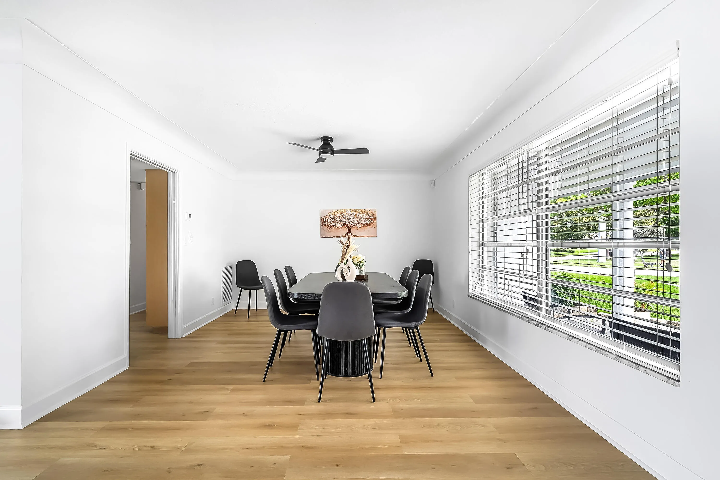 Bright interior space featuring wood-finish flooring, white walls, and a large window with horizontal blinds