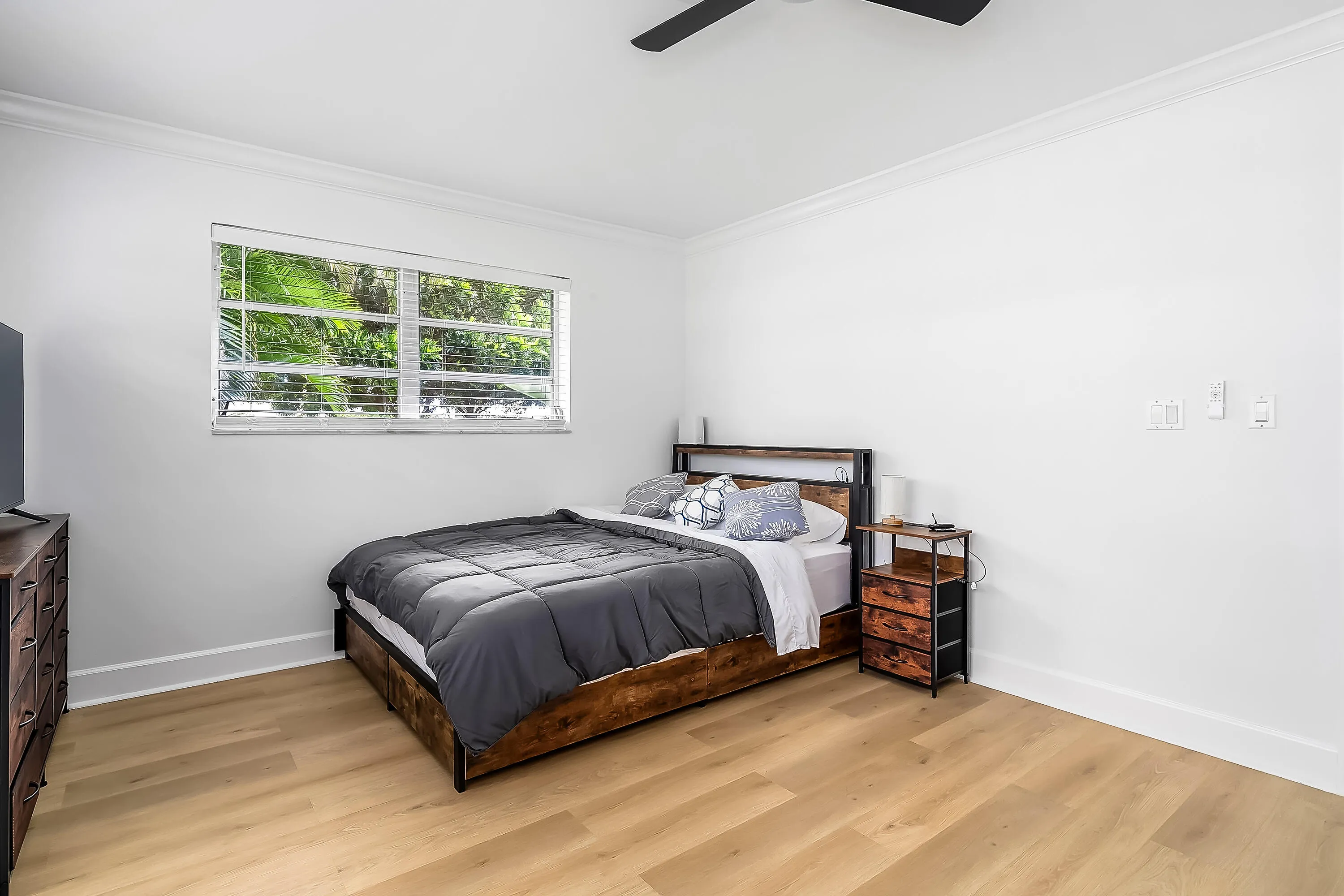 Spacious room featuring light wood-finish flooring, a window with horizontal blinds, crisp white walls, and crown molding
