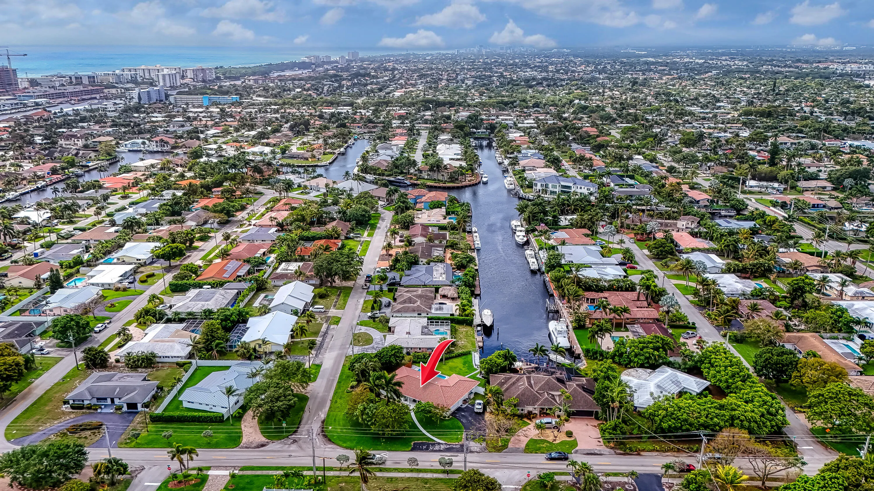 Aerial neighborhood overview with extensive canal system, residential properties, manicured landscaping, and distant ocean presence