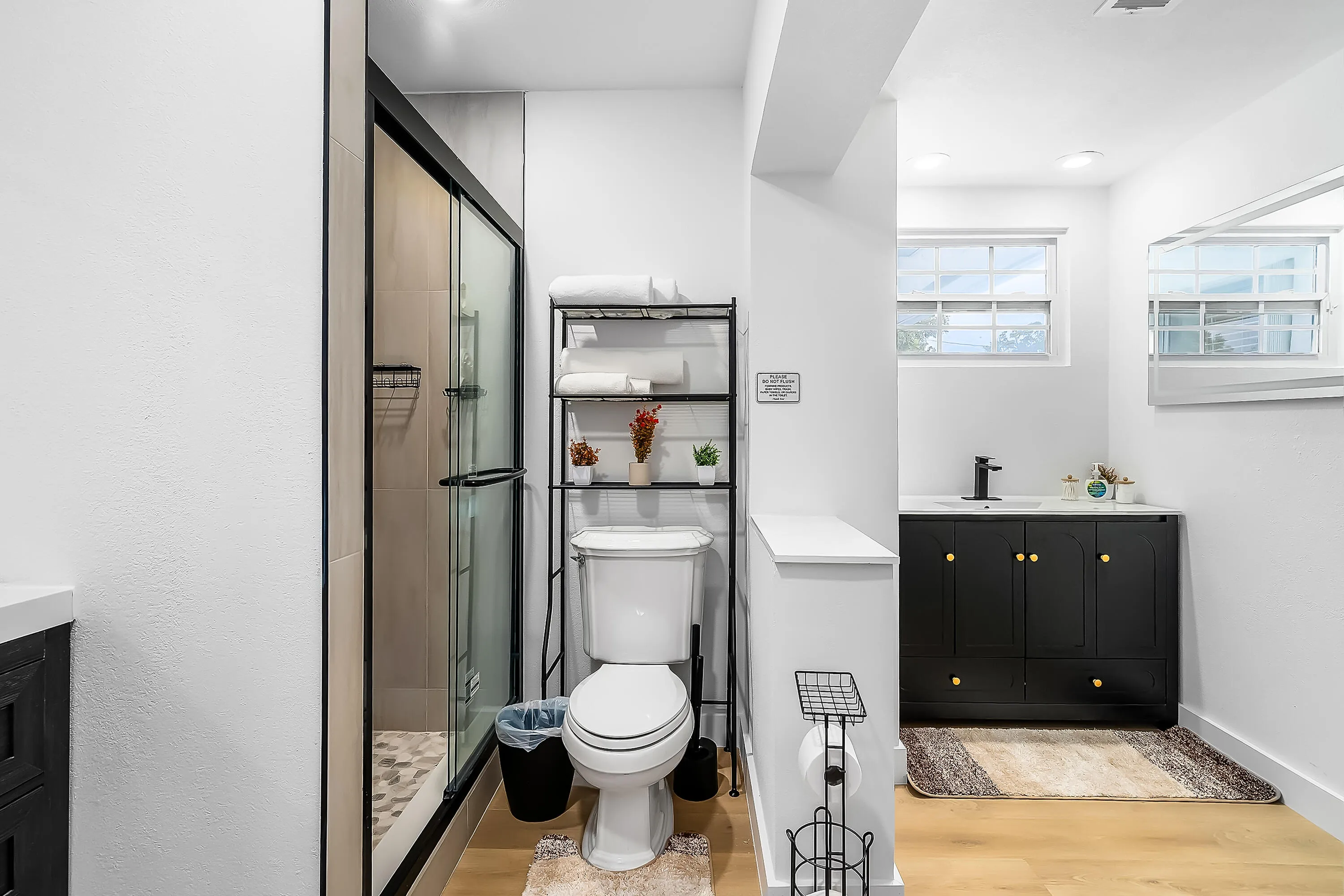 Shower with black-framed glass enclosure, toilet, and black vanity with gold-tone hardware