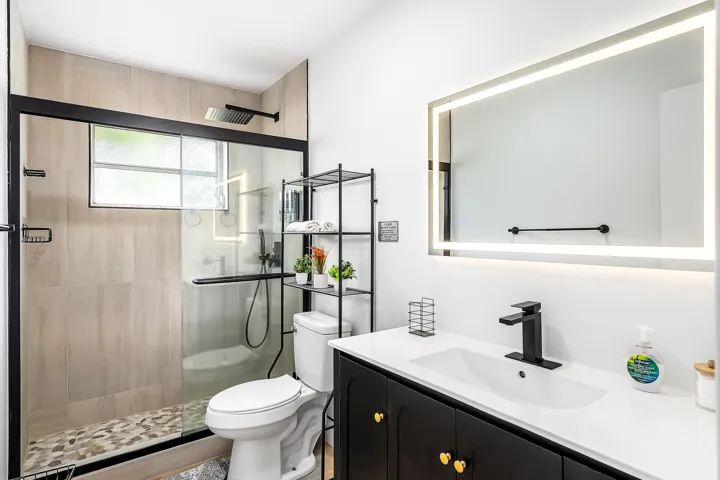 Contemporary bathroom featuring an illuminated vanity mirror, a black single-handle faucet, and a black vanity with gold-tone hardware