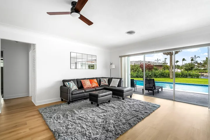 Bright living space featuring expansive sliding glass doors, light wood-finish flooring, and a contemporary ceiling fan