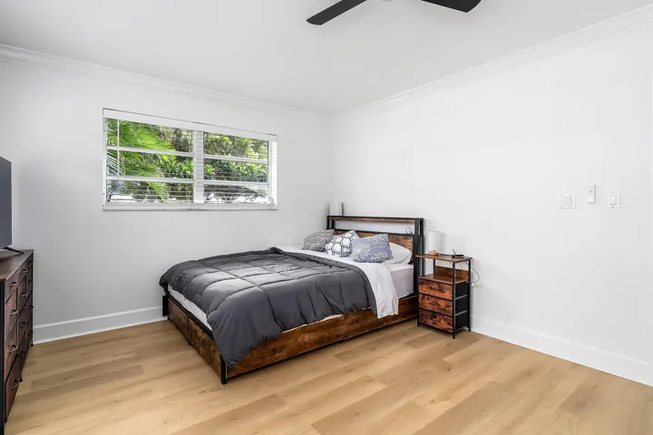 Spacious room featuring light wood-finish flooring, a window with horizontal blinds, crisp white walls, and crown molding