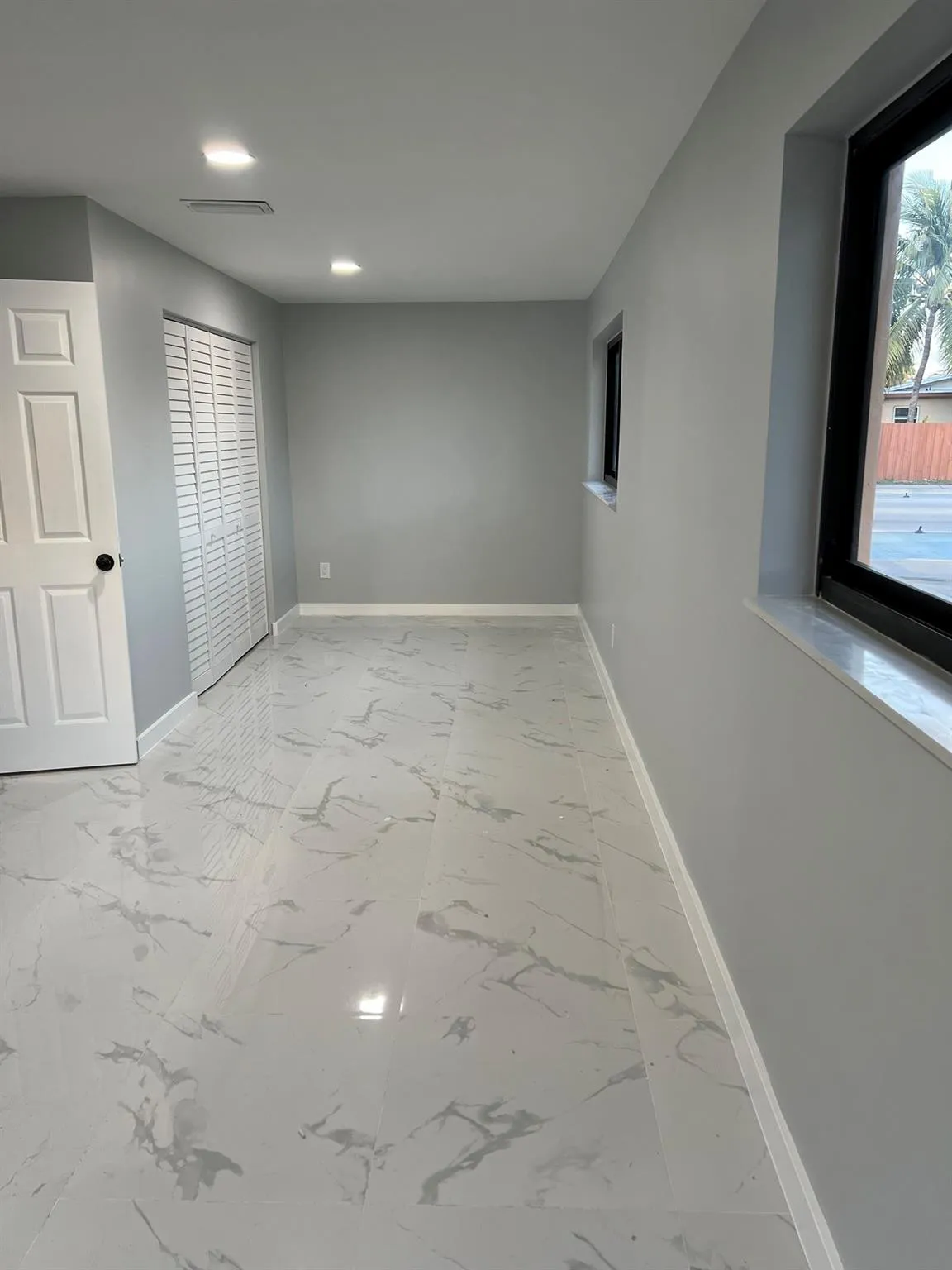 Recessed lighting, light gray wall finishes, white panel door, white louvered bifold closet doors, and marble-look tile flooring
