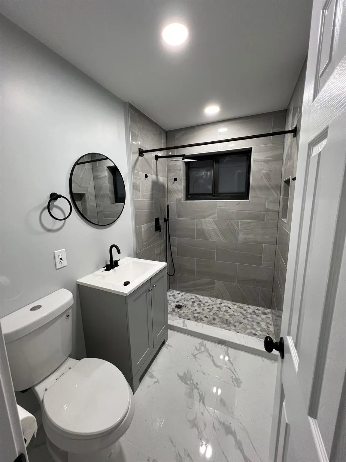 Vanity with integrated sink, black fixtures, tiled shower with pebble floor, and large format floor tiling