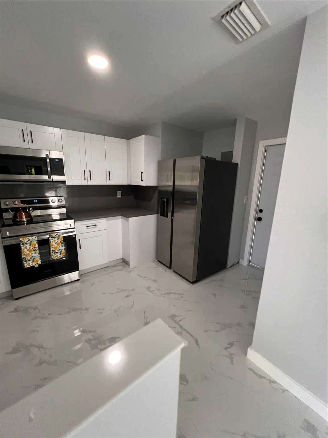 Kitchen featuring white cabinetry, stainless steel appliances, dark countertops, and light-toned flooring