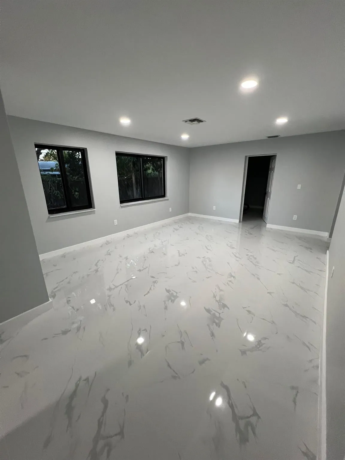 Recessed lighting illuminates the spacious room, featuring two windows with dark frames and white sills