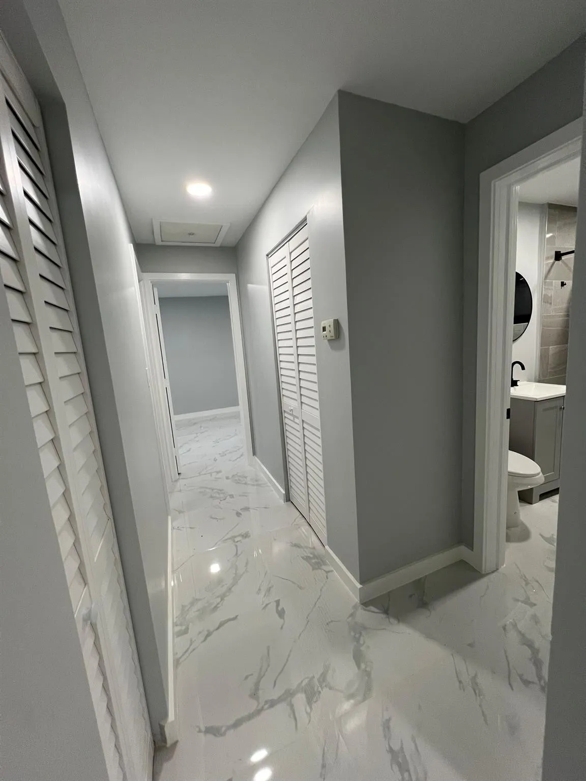 Hallway featuring white marble-look flooring, recessed lighting, and louvered closet doors