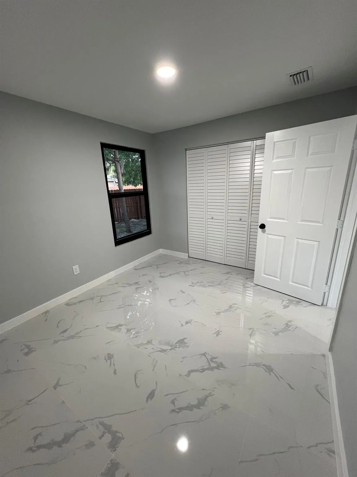 Recessed ceiling lighting illuminates the room, featuring light gray walls and white marble-look flooring