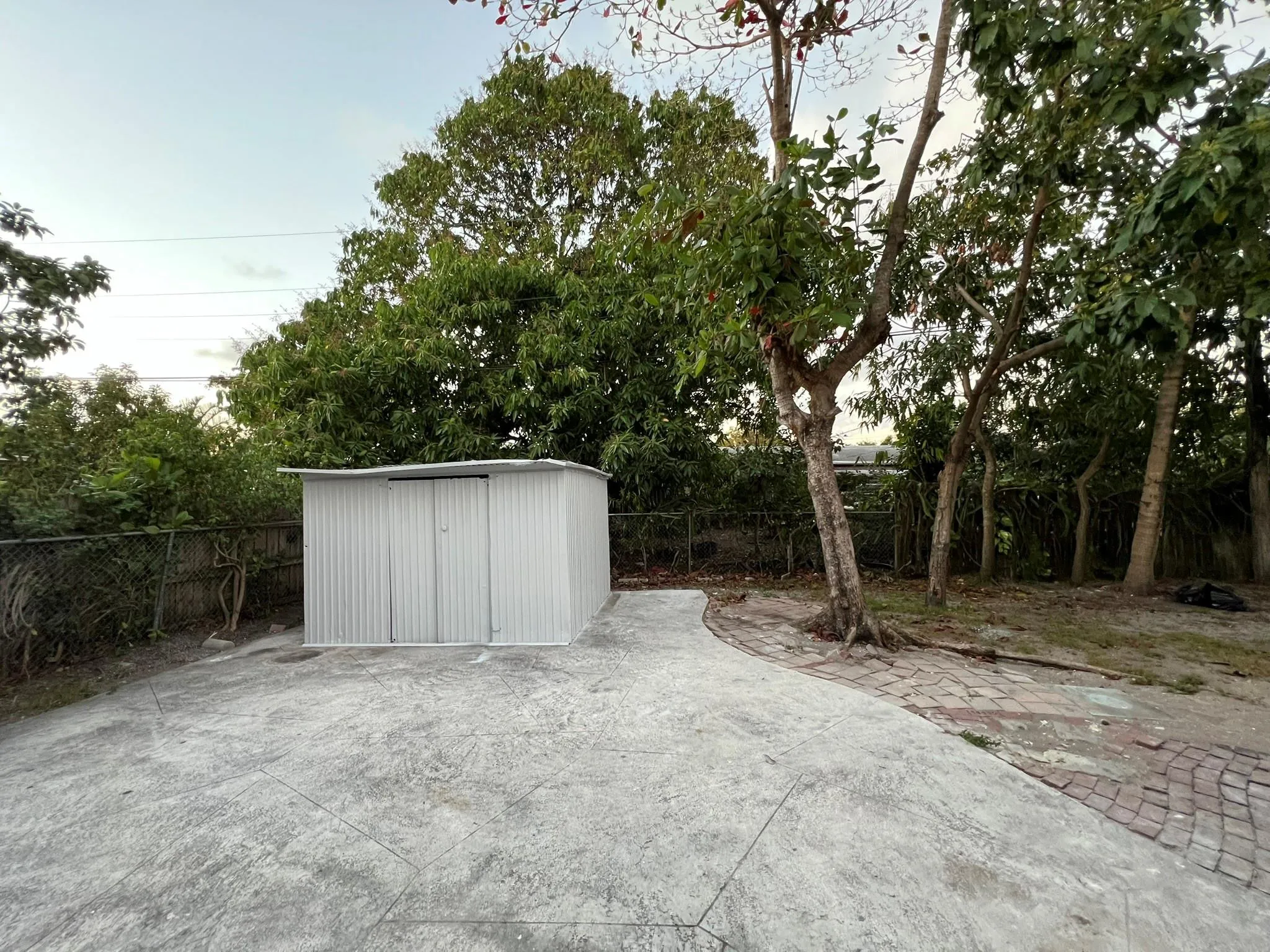 Detached storage shed, paved surface, mature trees, chain link fencing, natural landscaping