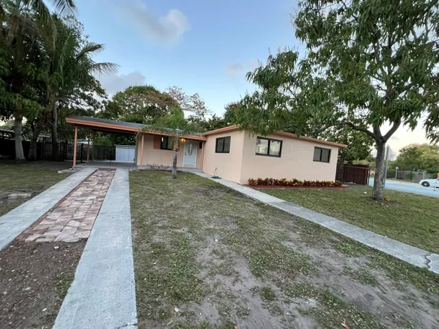 Stucco exterior with dark-framed windows, a covered carport, and a paver-lined driveway