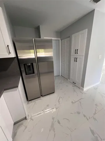Stainless steel side-by-side refrigerator, white flat-panel cabinetry, dark countertops, white tile flooring, and a built-in pantry with shaker-style doors
