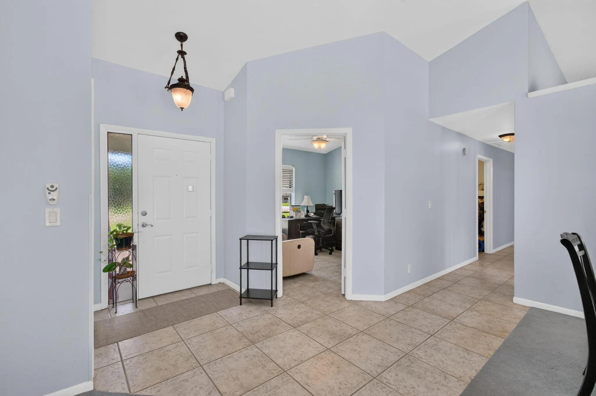 Foyer with tile flooring, vaulted ceilings, a decorative pendant light fixture, and a white front door with a textured glass sidelight
