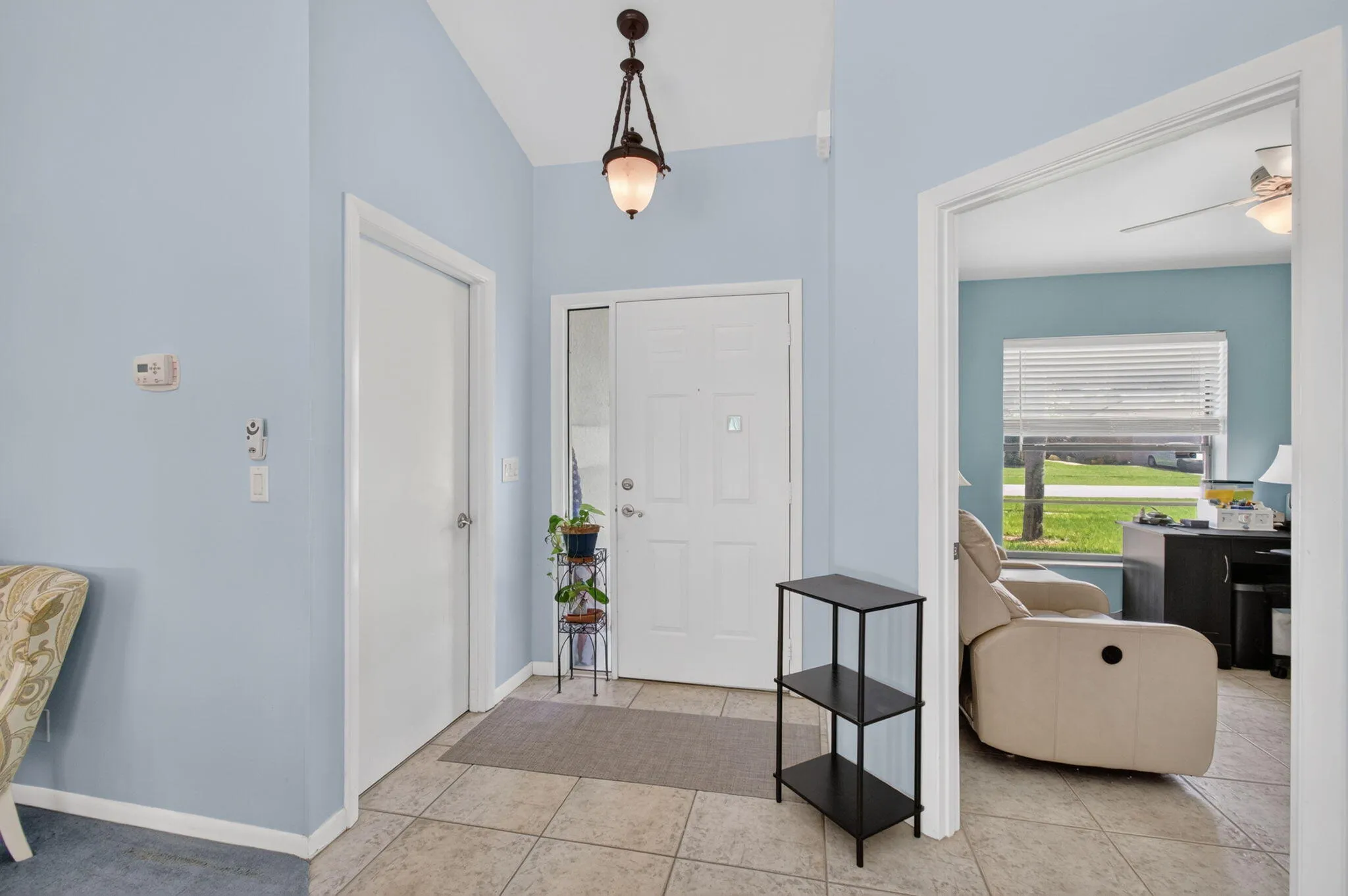 Vaulted entry ceiling with decorative hanging fixture, tile flooring, and a sidelight window