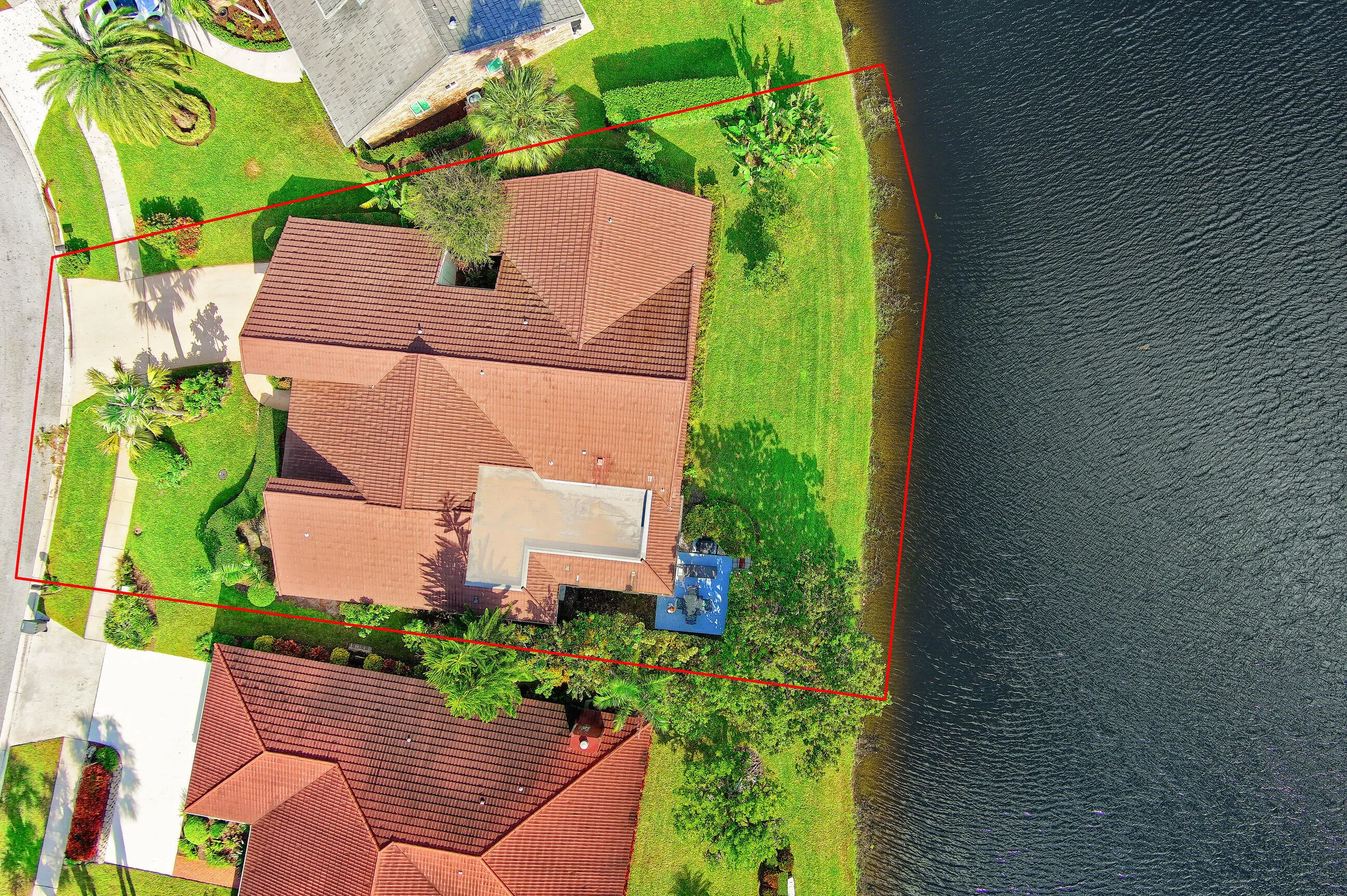 Waterfront property with a tile roof, mature landscaping, a paved driveway, and manicured lawns