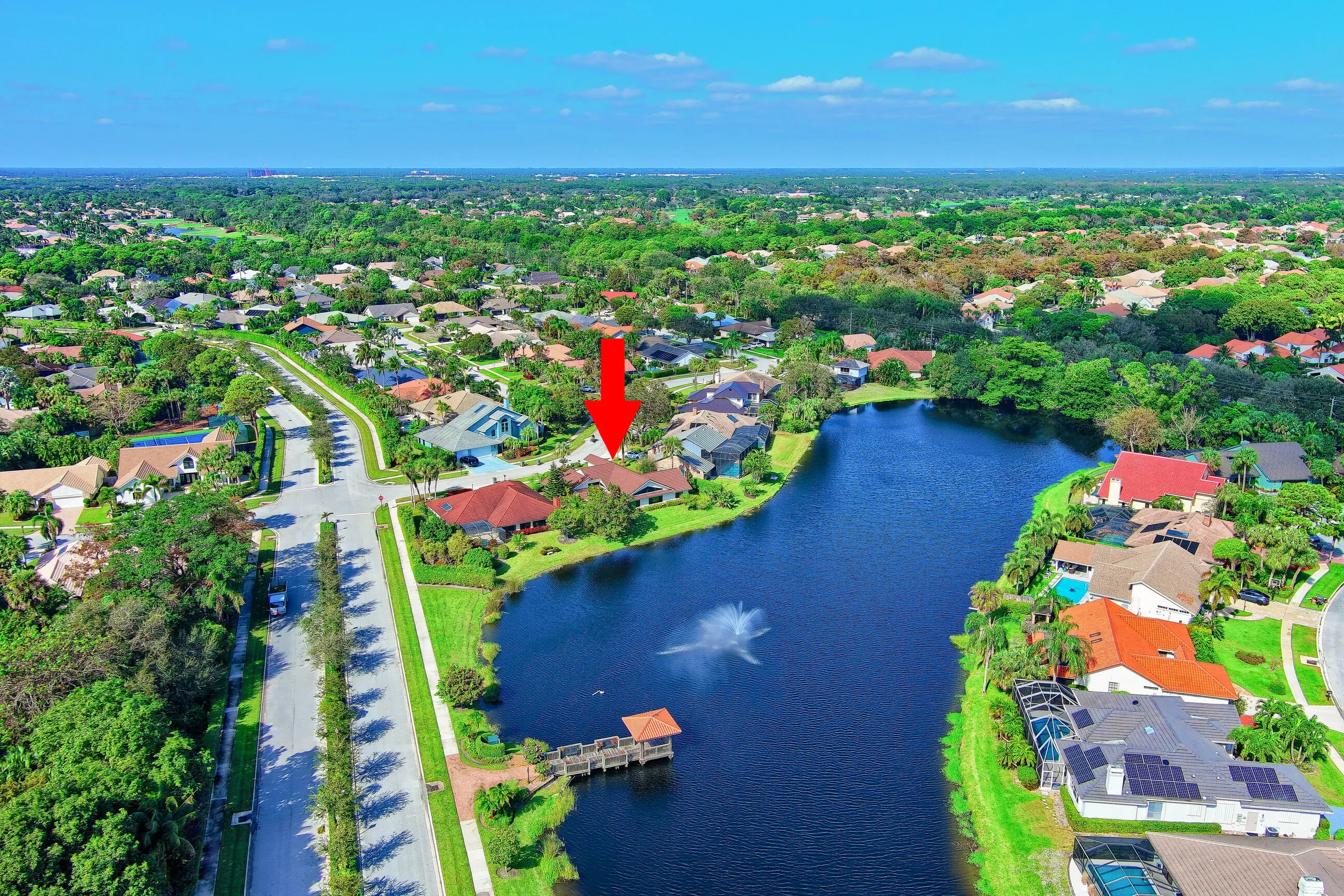 Lakeside property featuring a boat dock, expansive body of water with a fountain, and lush surrounding greenery