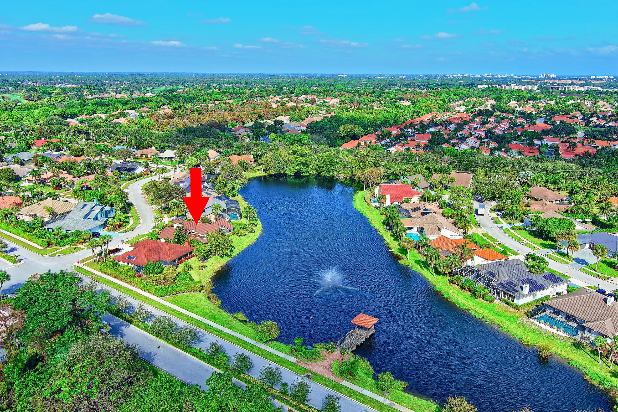 Lakeside property with a red tile roof, surrounded by mature trees, and a private swimming pool