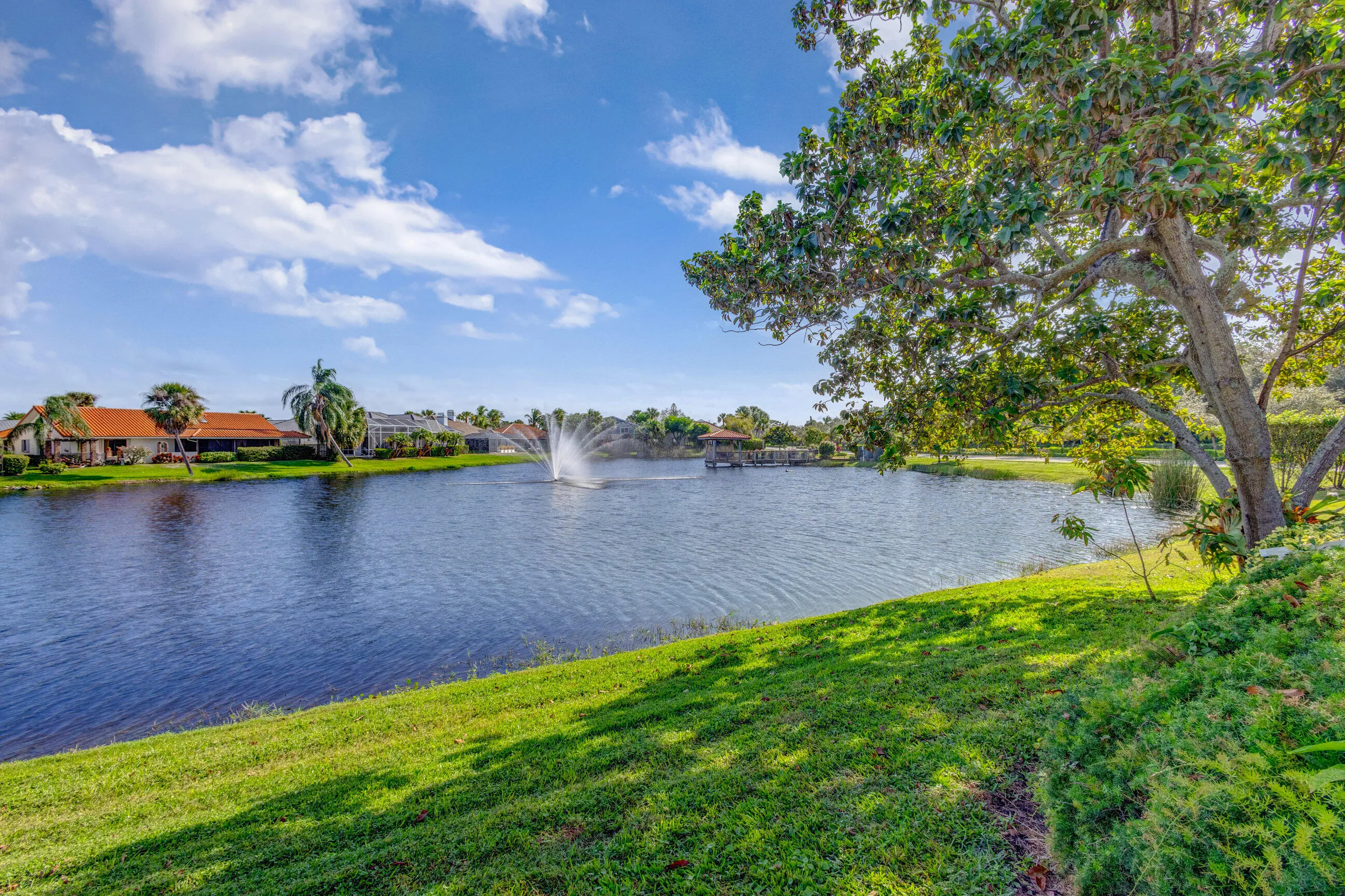 Waterfront property featuring a fountain, verdant landscaping, and mature trees