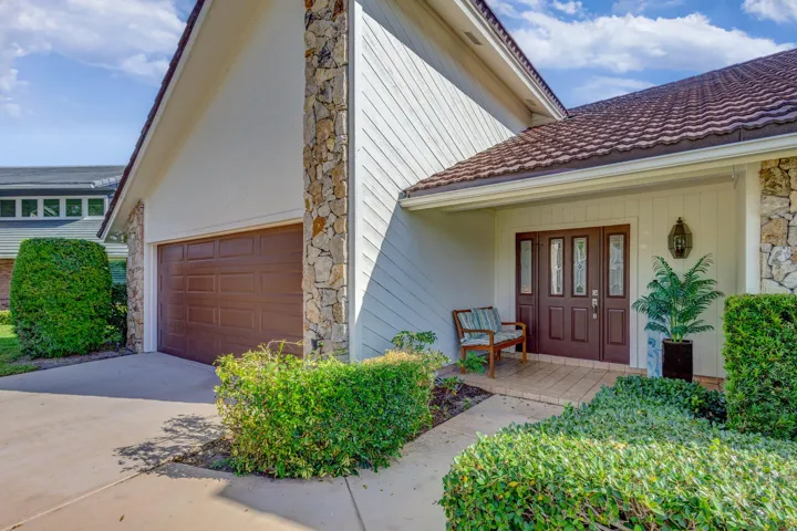 Stone facade accents, durable tile roofing, wood-paneled garage door, double entry doors with decorative glass, and a covered entry porch