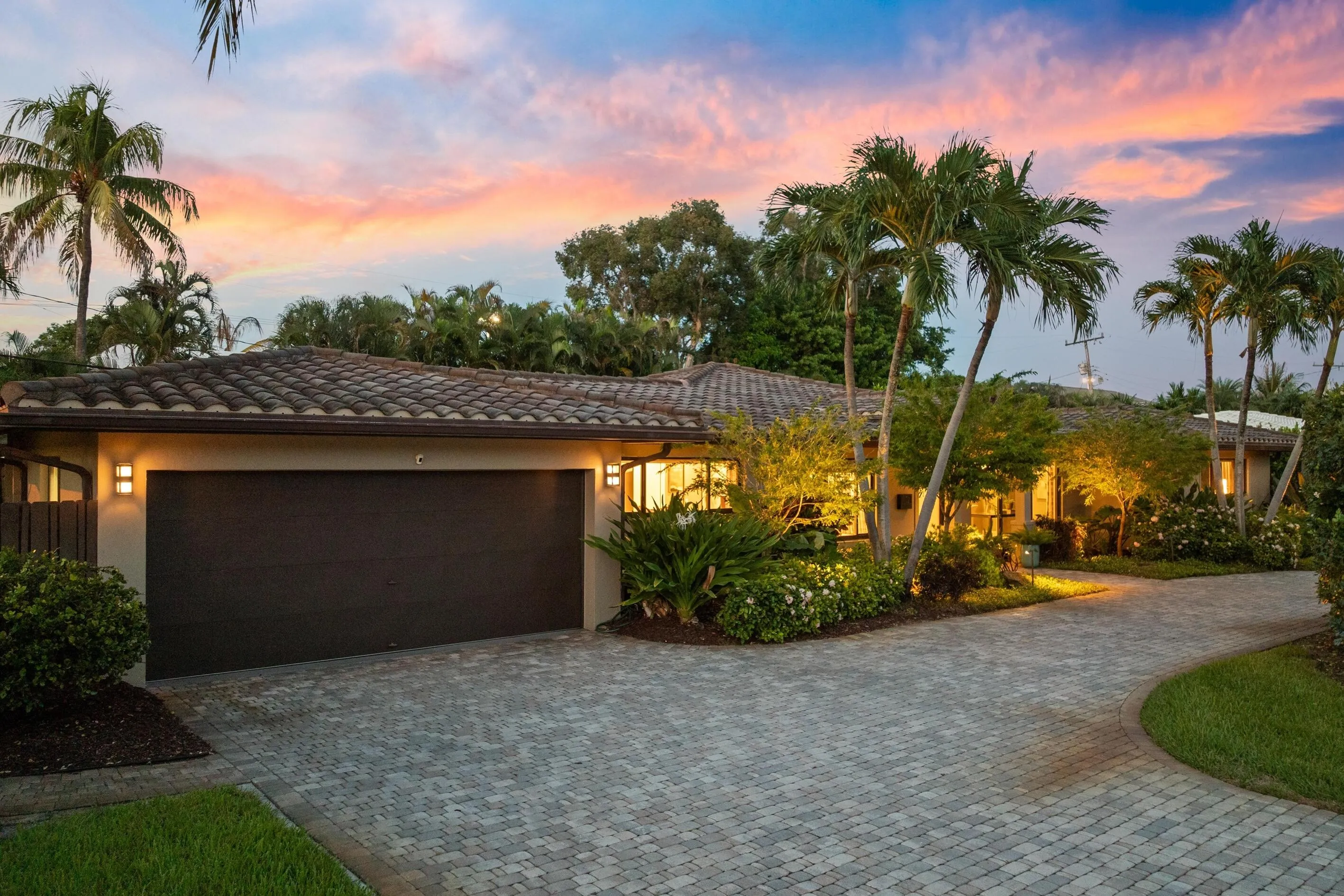 Tiled roof, paver driveway, mature palm trees, exterior lighting, and lush landscaping