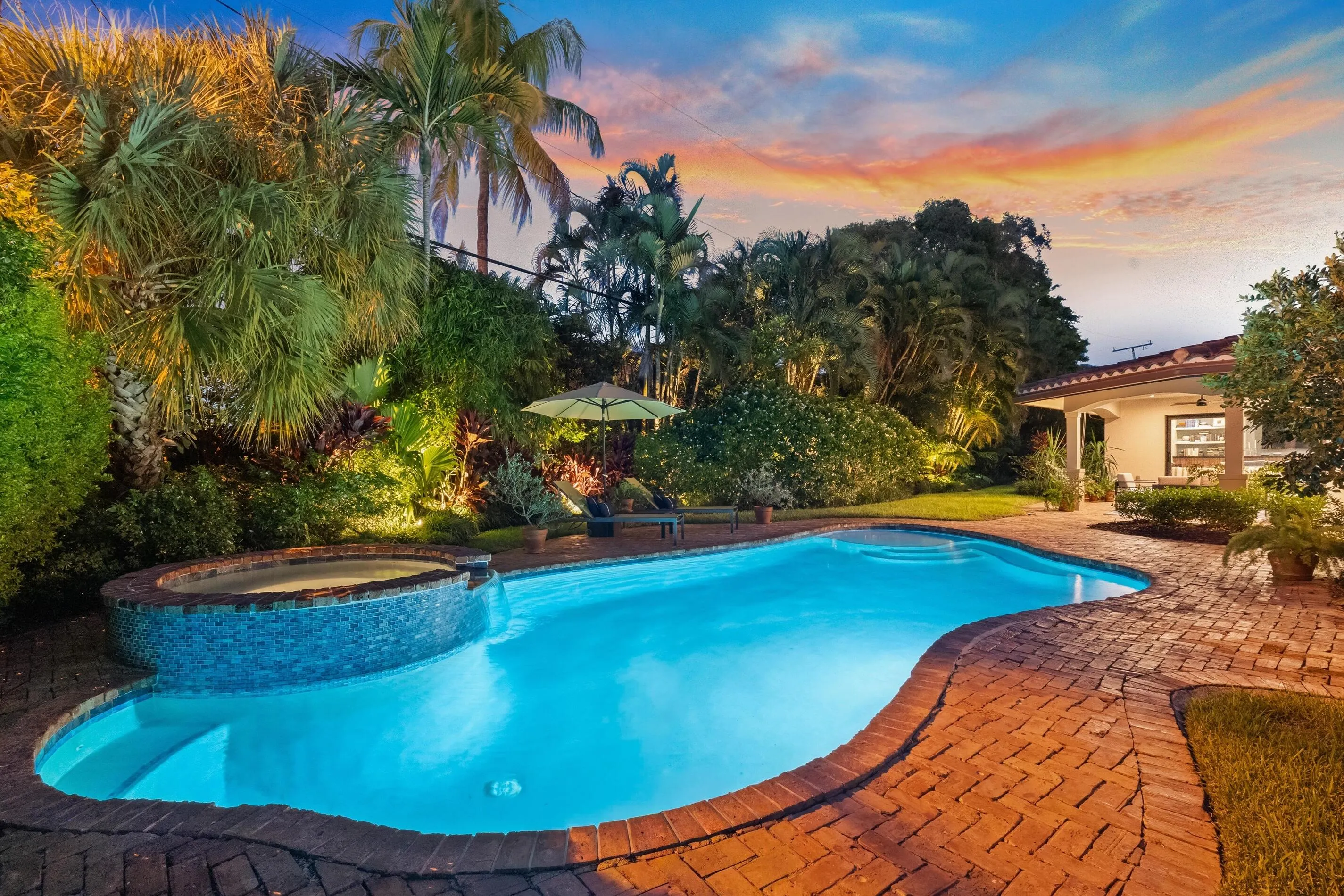 Freeform swimming pool with an integrated spa, surrounded by brick-paved decking