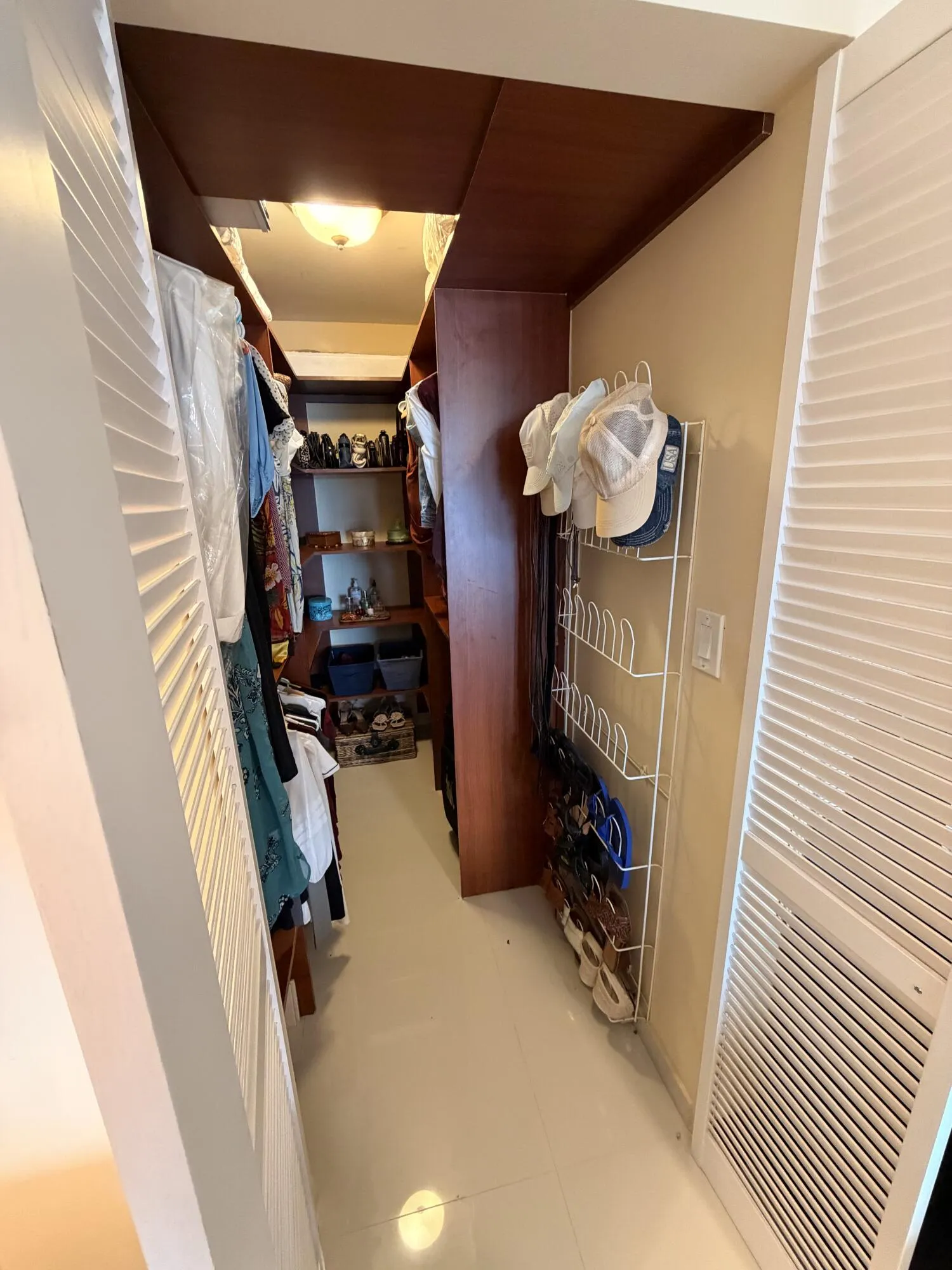 Walk-in closet featuring white flooring, built-in shelving, and louvered bifold doors