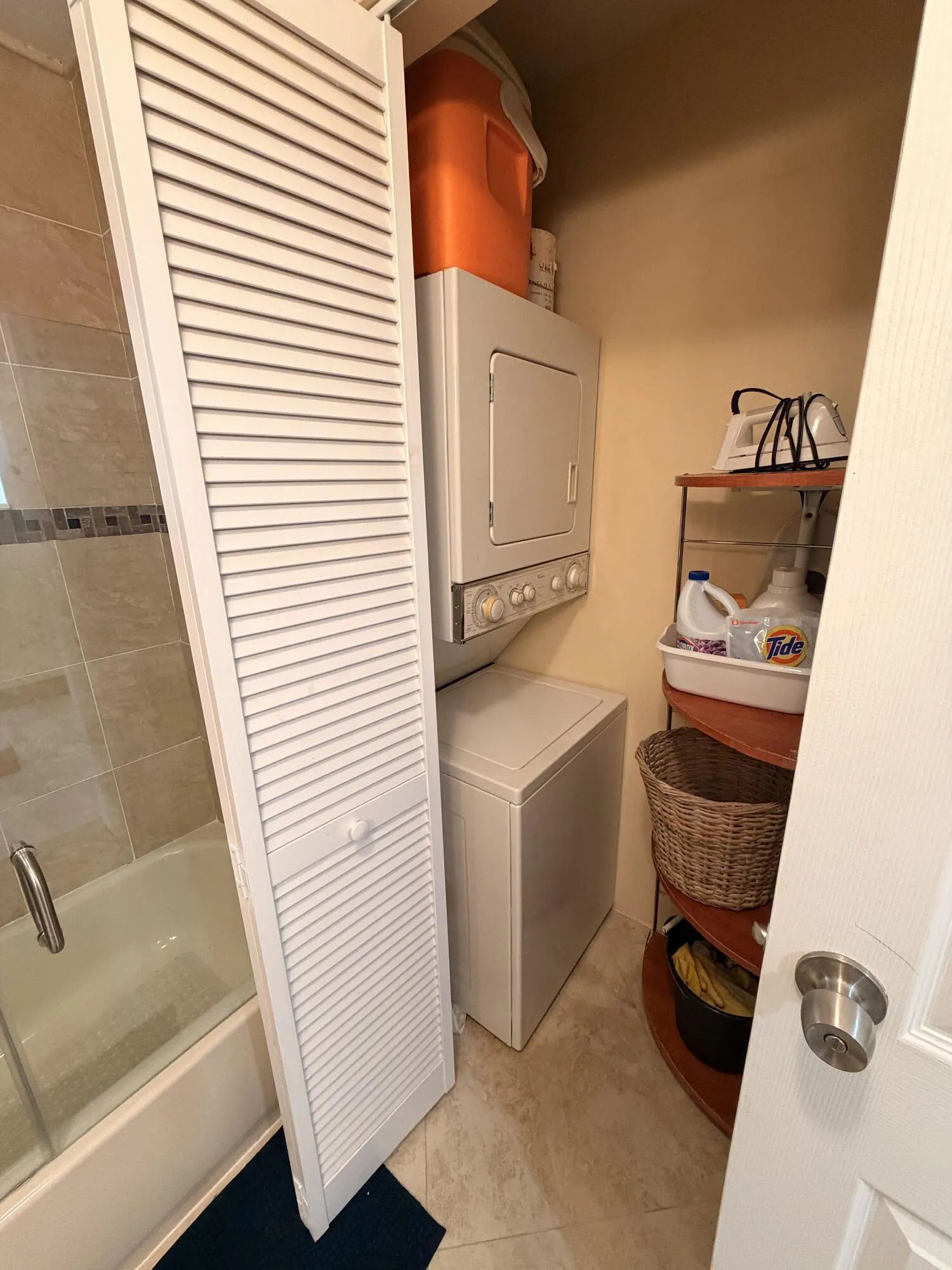 Stacked washer and dryer unit, louvered bi-fold door, and tiled flooring