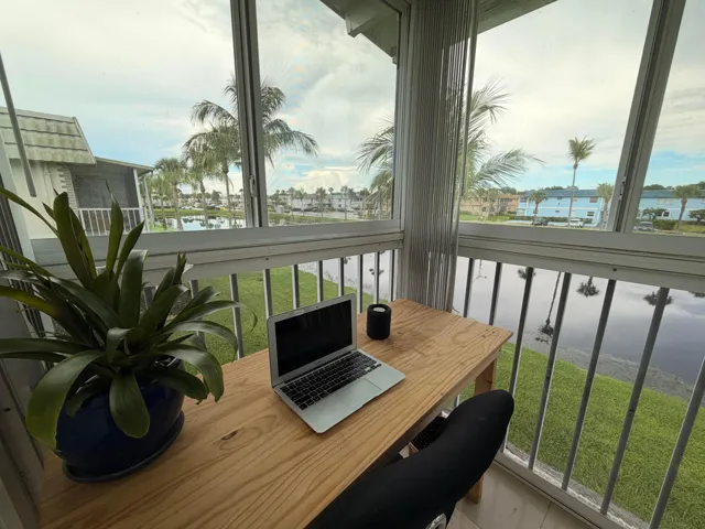 Enclosed balcony featuring large windows, a natural wood-finish desk, and water scenery