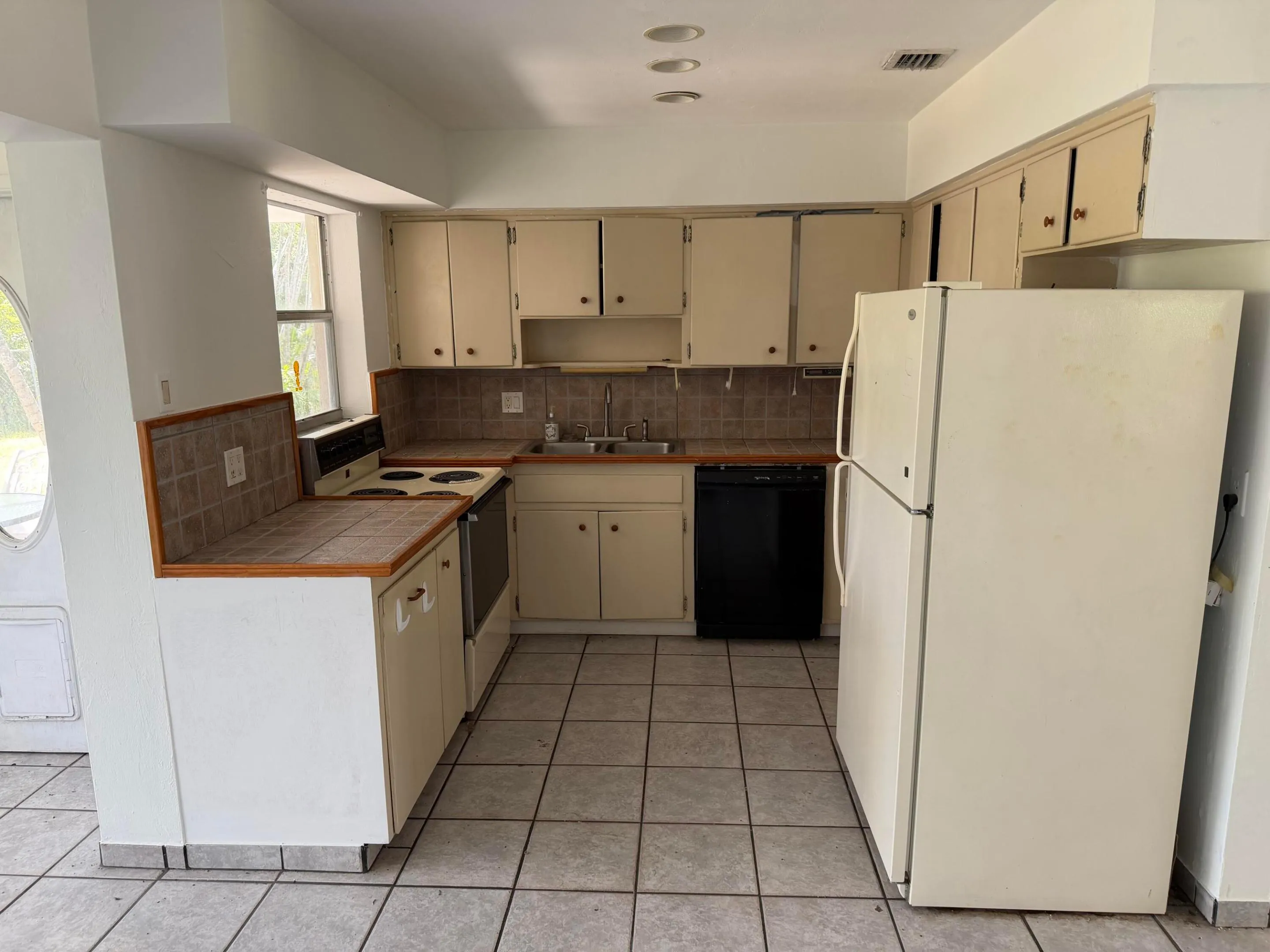 U-shaped kitchen layout featuring tile flooring, white cabinetry, a double-basin sink, and a black dishwasher