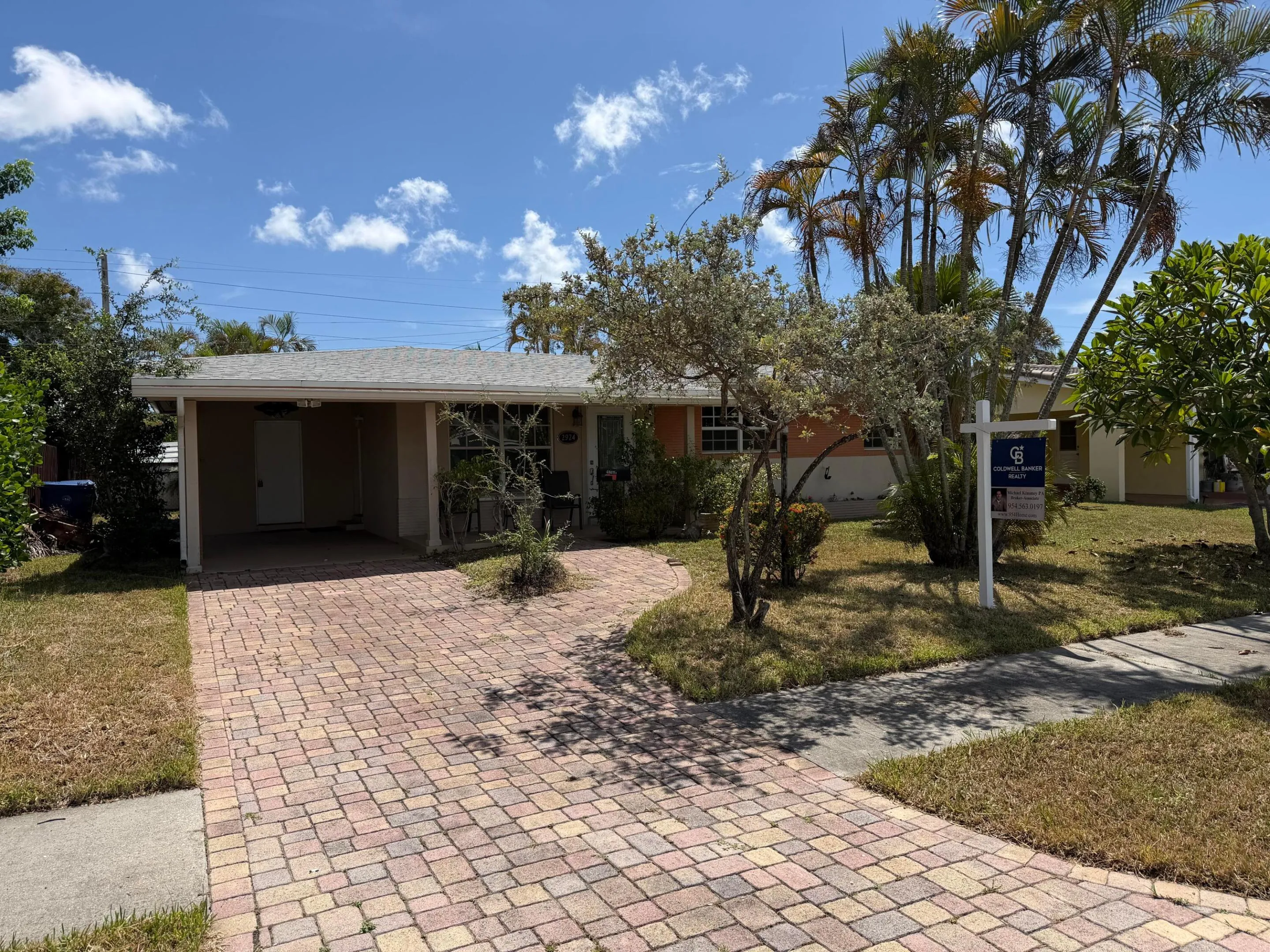 Single-story residence featuring a covered carport, brick paver driveway, and mature palm trees