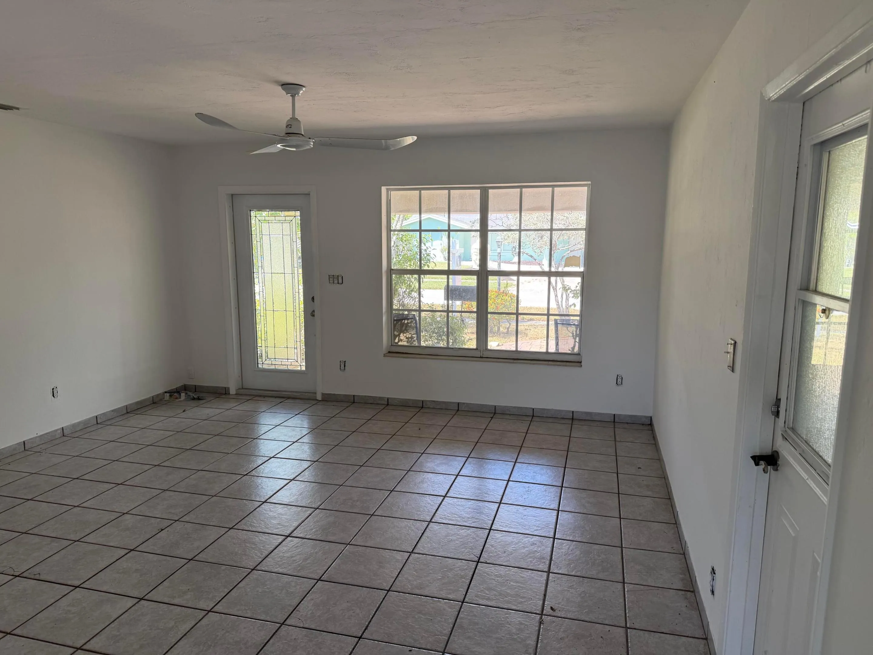Ceramic tile flooring, white painted walls, ceiling fan, multiple windows for ample light, and a glass-paneled exterior door