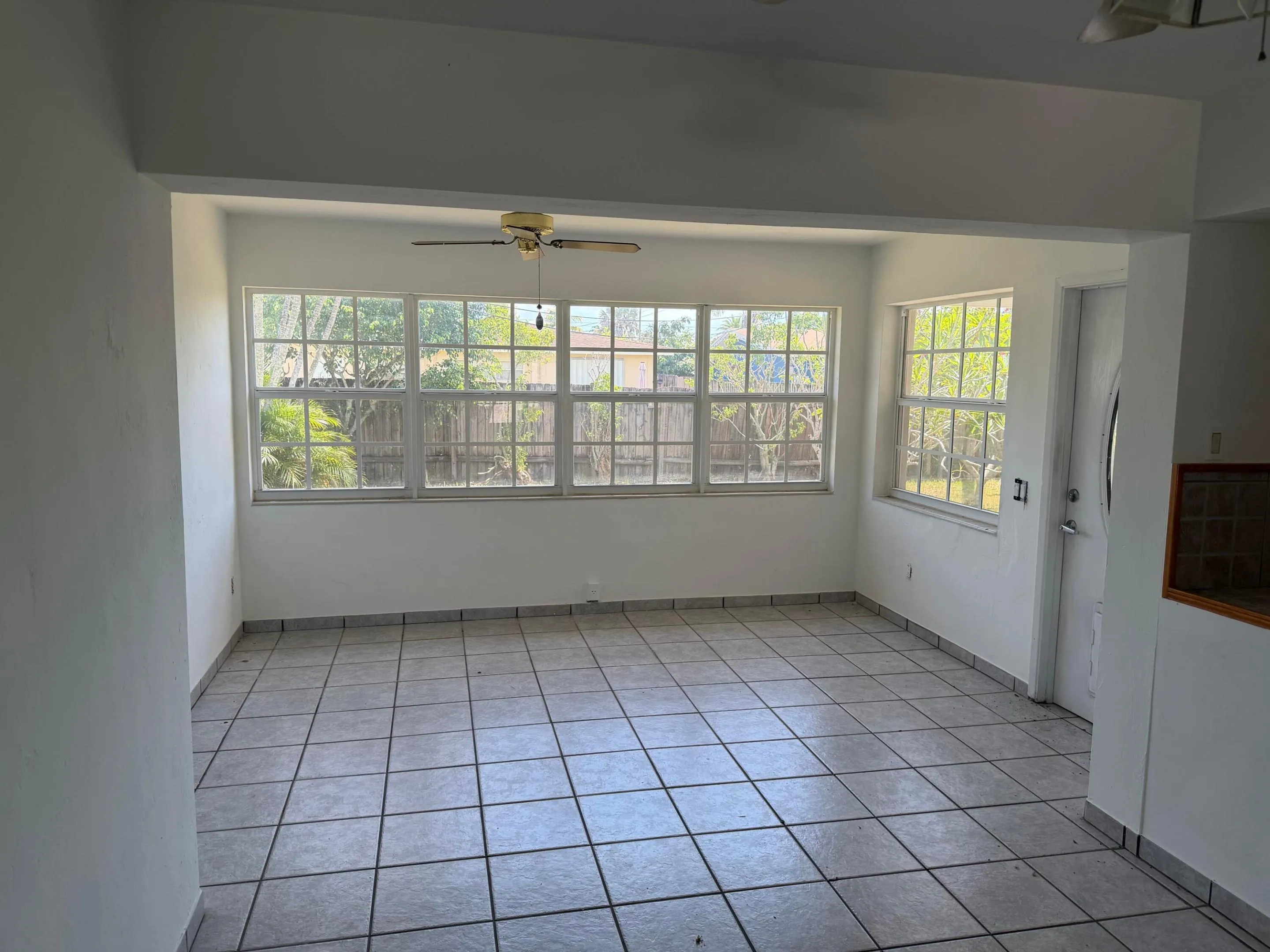 Tiled flooring, multiple windows, ceiling fan, white walls, and a perimeter fence