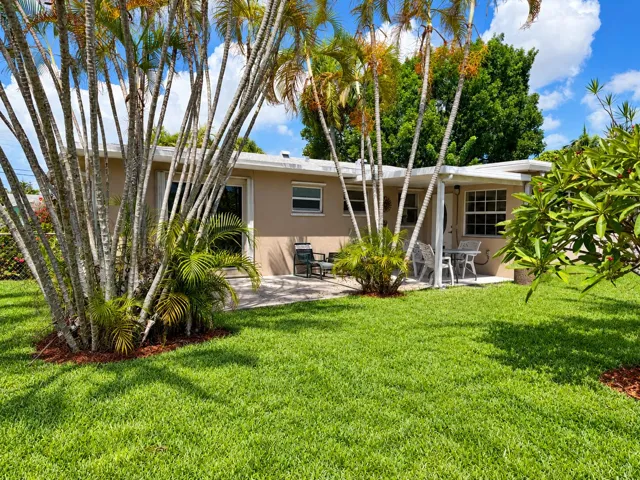 Rear exterior with a concrete patio, covered porch area, and mature palm trees