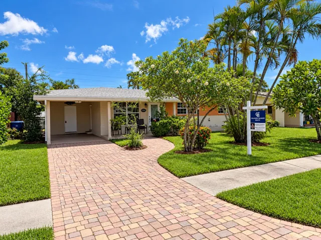 Single-story residence featuring a covered carport, brick paver driveway, and mature palm trees